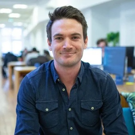 Smiling man seated at digital solution workspace, engaging with content and editorial publishing workflow.