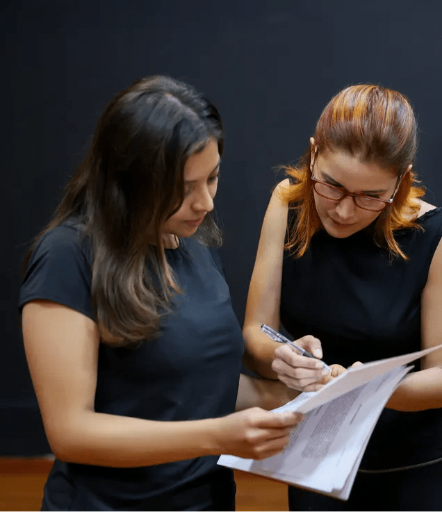 Two colleagues reviewing a printed document together, with one person making notes while the other holds the pages.