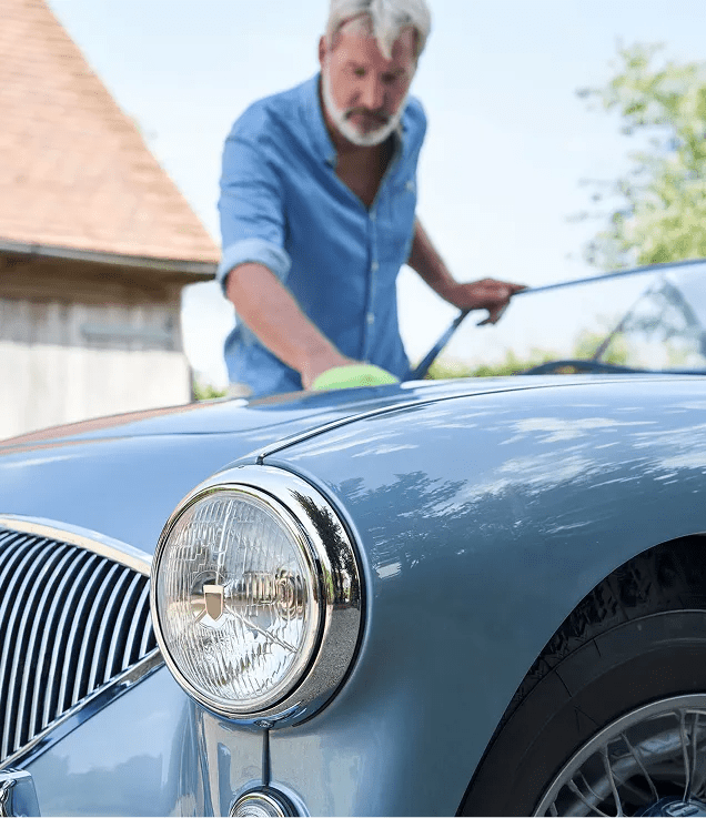 Close-up of a vintage car while a person polishes the hood.