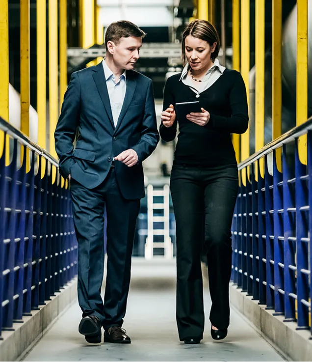 Two professionals walking through an industrial facility while reviewing information on a tablet.