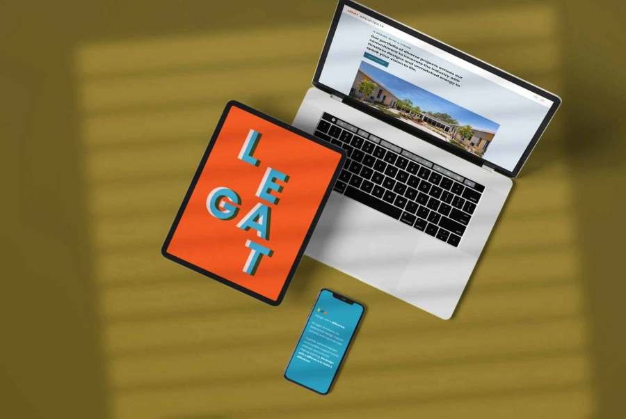 Laptop, tablet with text LEAGAT, and smartphone on a yellow surface with shadow lines.