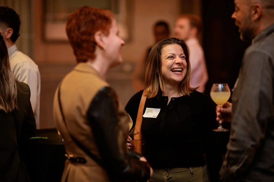 A woman laughs and chats with others at an Innovation Exchange event; one person holds a drink.