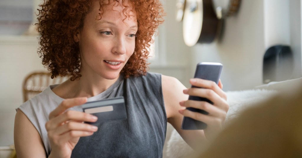 A person looking at their phone and holding up their credit card