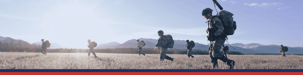 Soldiers with packs walking across a field. 